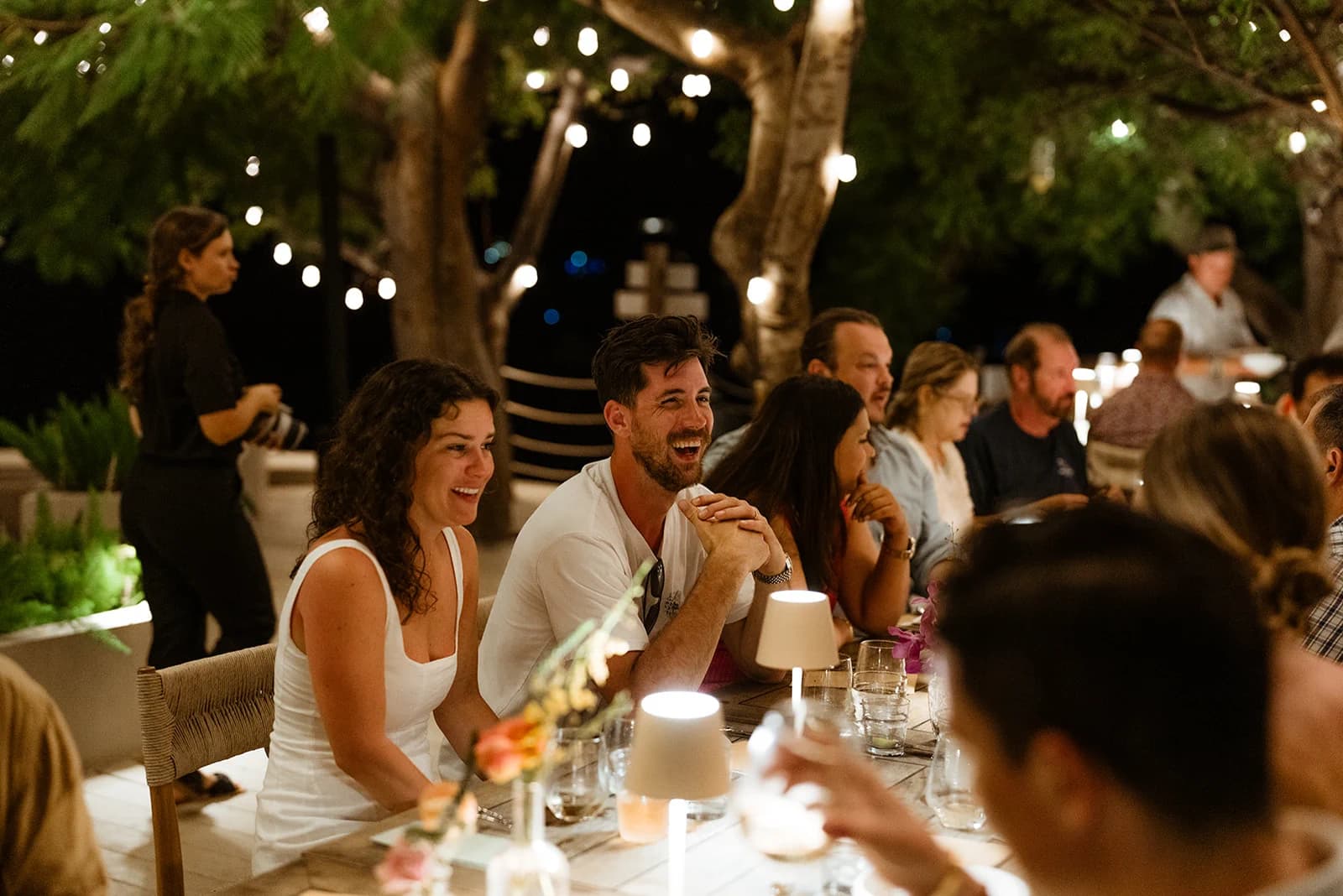 Guests sharing a candlelit alfresco dinner under string lights