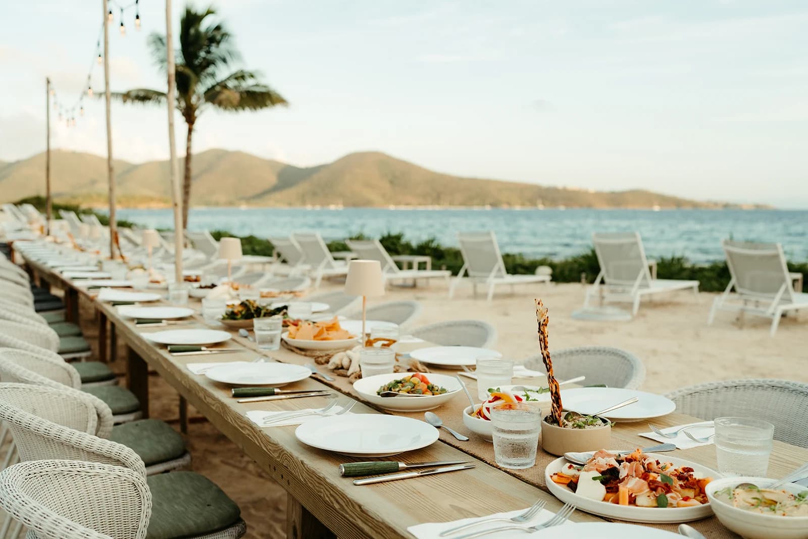 A beachfront long-table dinner at golden hour, set against the ocean and palms